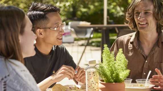 Net Zero environment with 3 young people smiling and chatting while having a meal.