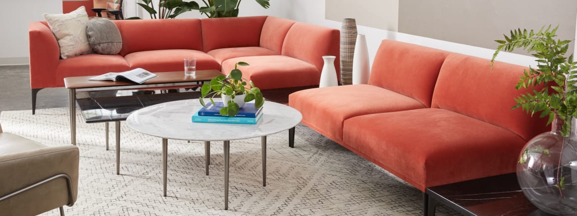 A West Elm Work Mesa sectional sofa with orange upholstery shown with West Elm Work tables in an office lounge setting